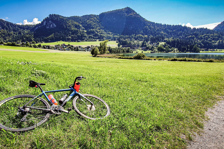Fahrrad liegt auf einer Wiese mit den Alpen im Hintergrund.